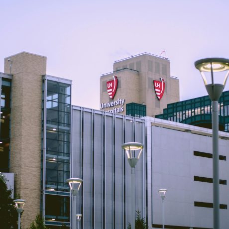 University Hospitals building exterior at dusk with red shield logos on upper facade and street lamps in foreground