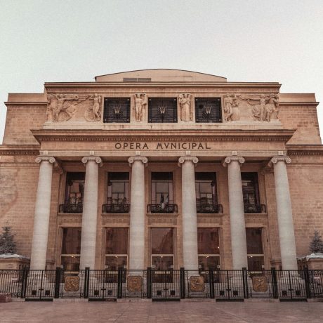 Opera Municipal building facade with classical columns, stone relief sculptures, and iron fence, viewed from plaza