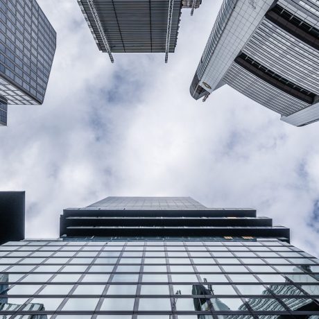 Upward view between tall glass and steel office towers against a cloudy sky