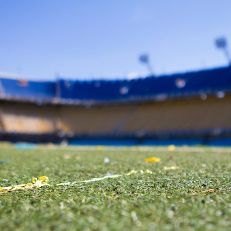 Ground-level view of grass field with yellow confetti scraps inside an empty stadium with blue and yellow seating