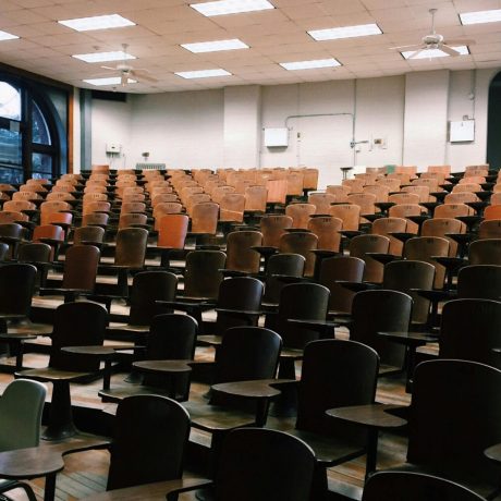Empty university lecture hall with rows of numbered wooden tablet-arm chairs on a tiered floor